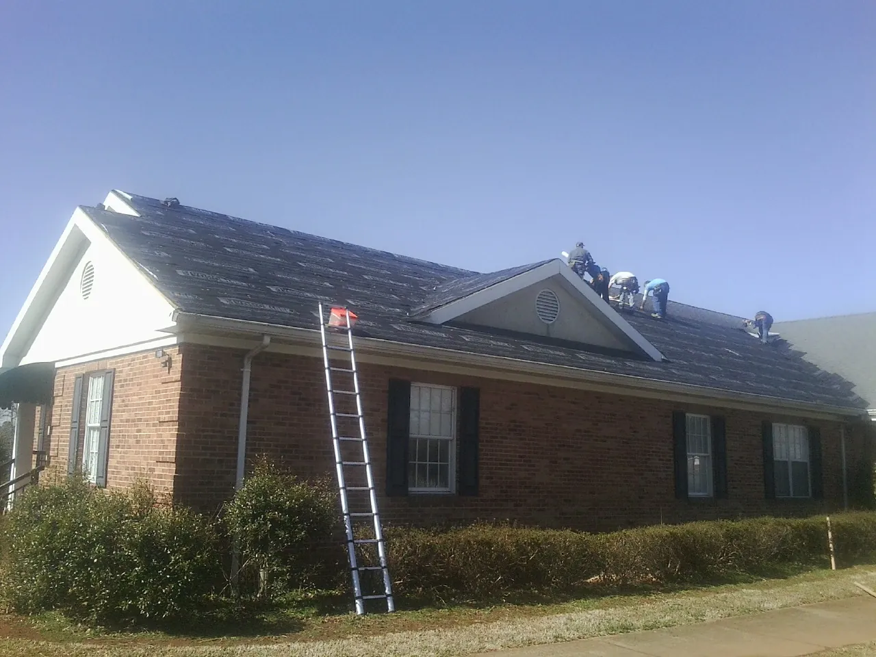 Crew tearing shingles off a brick ranch roof with a ladder set — Emergency Roof Repair work by our crew in Upperstrasburg