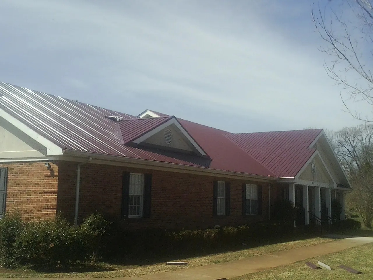 Red metal roof with gabled entries on a long brick building, from a Hail Damage Roof Repair job in Upperstrasburg