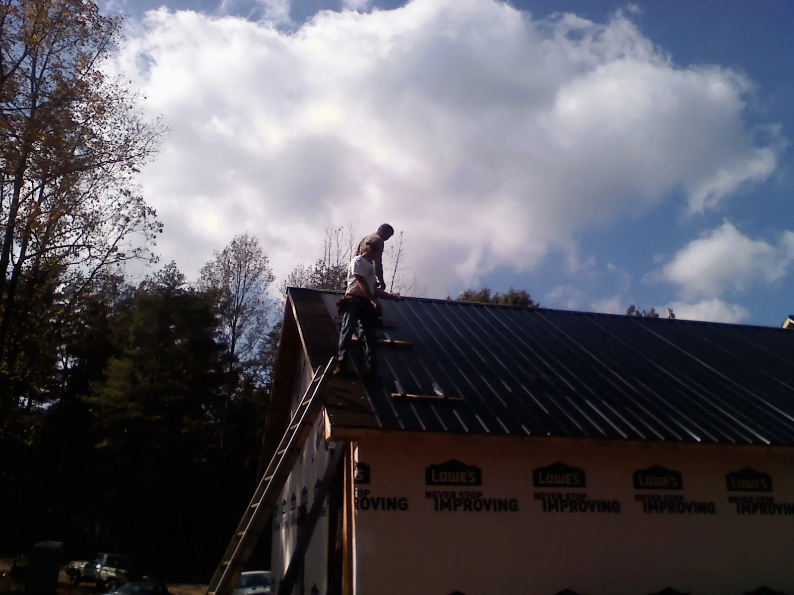 Roofer fastening dark metal panels high against a cloudy sky, from a Roof Inspection job in Upperstrasburg