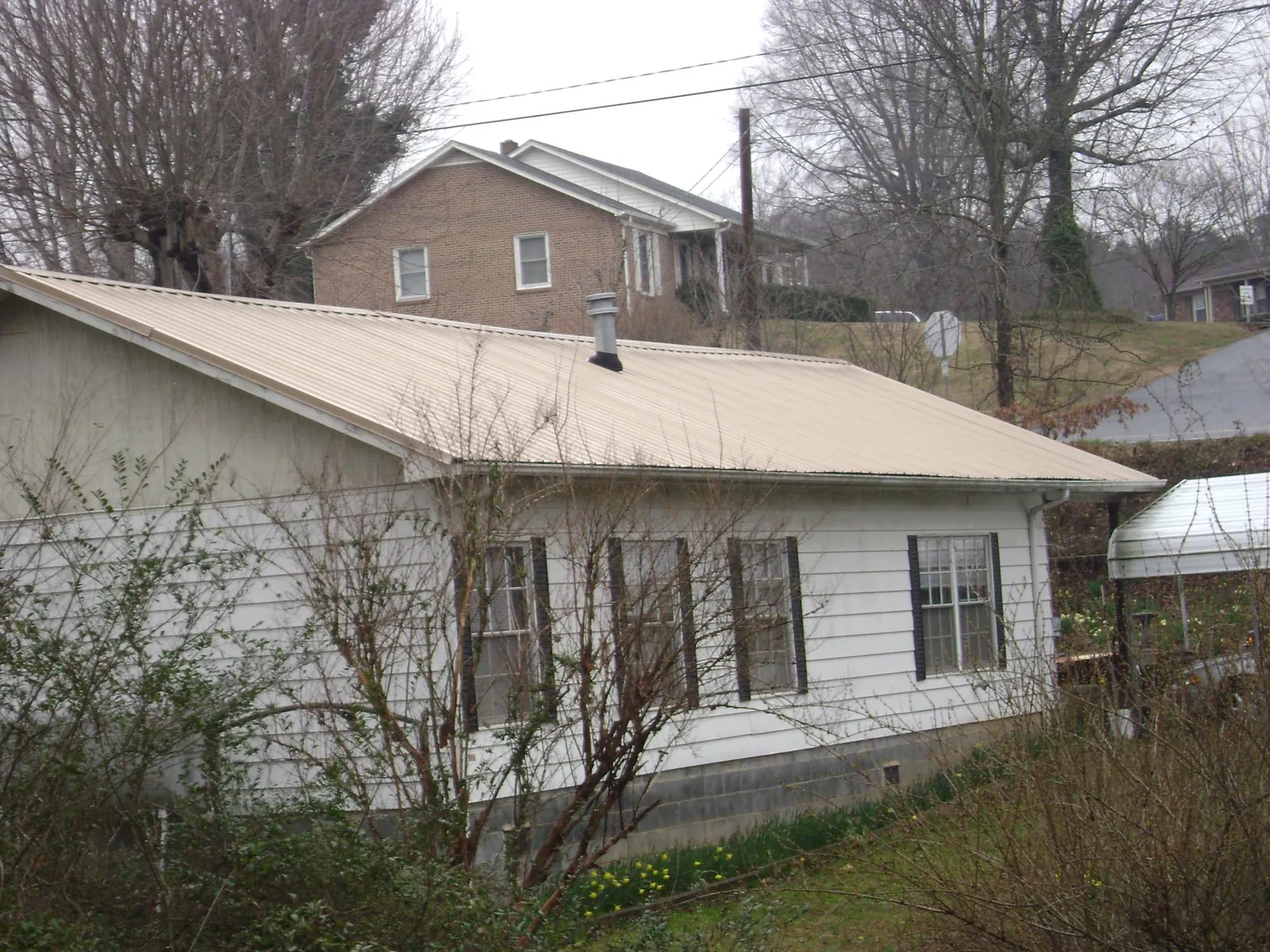 Tan metal roof on a white sided house set into a hillside — Commercial Roofing by Roofing Brothers in Upperstrasburg